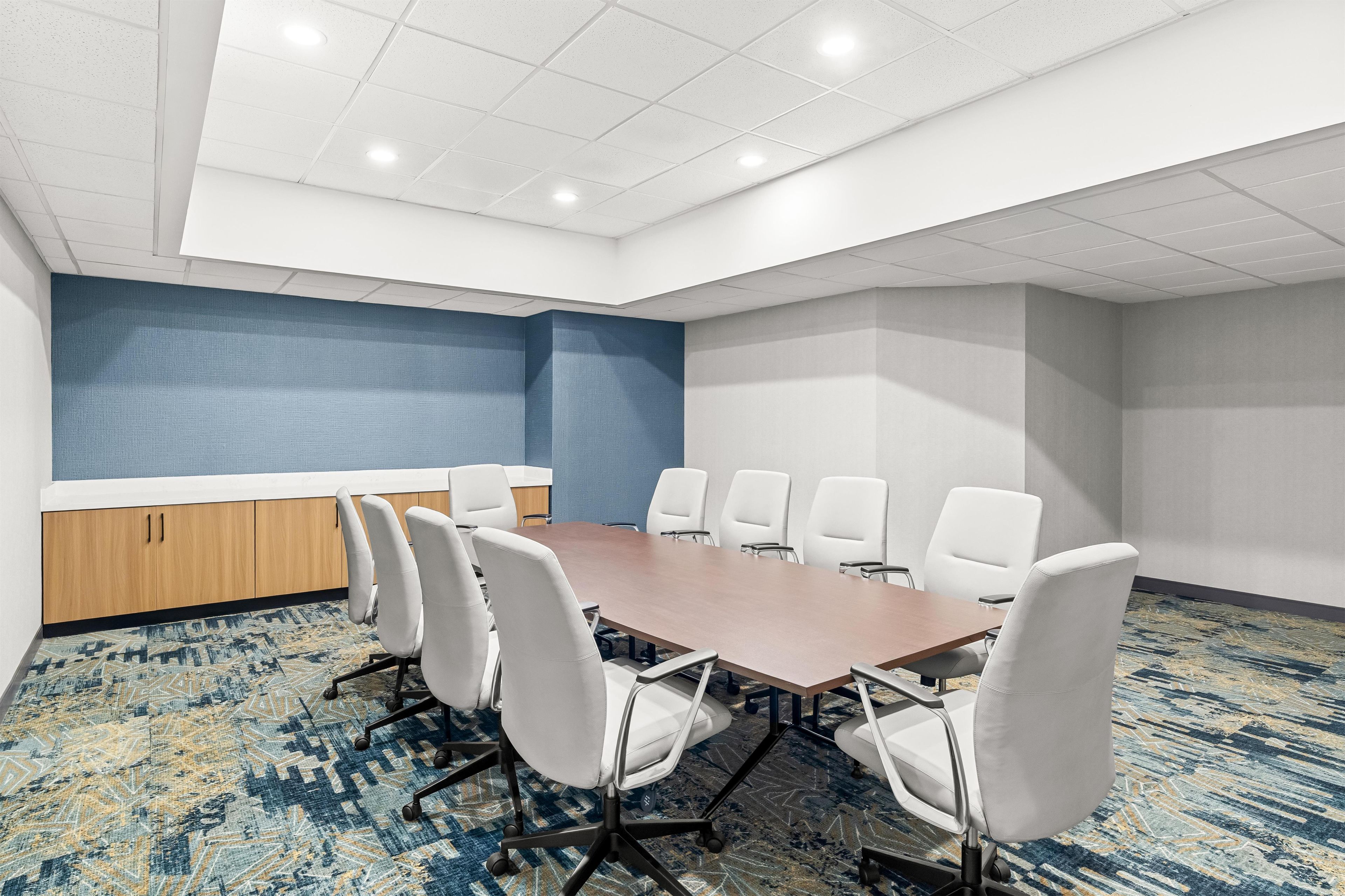 A conference room with a long table, white chairs, a blue accent wall, and a patterned carpet.