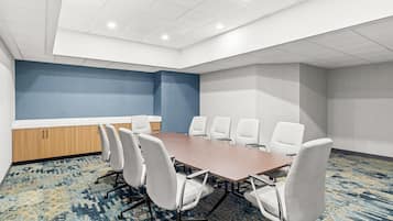A conference room with a long table, white chairs, a blue accent wall, and a patterned carpet.