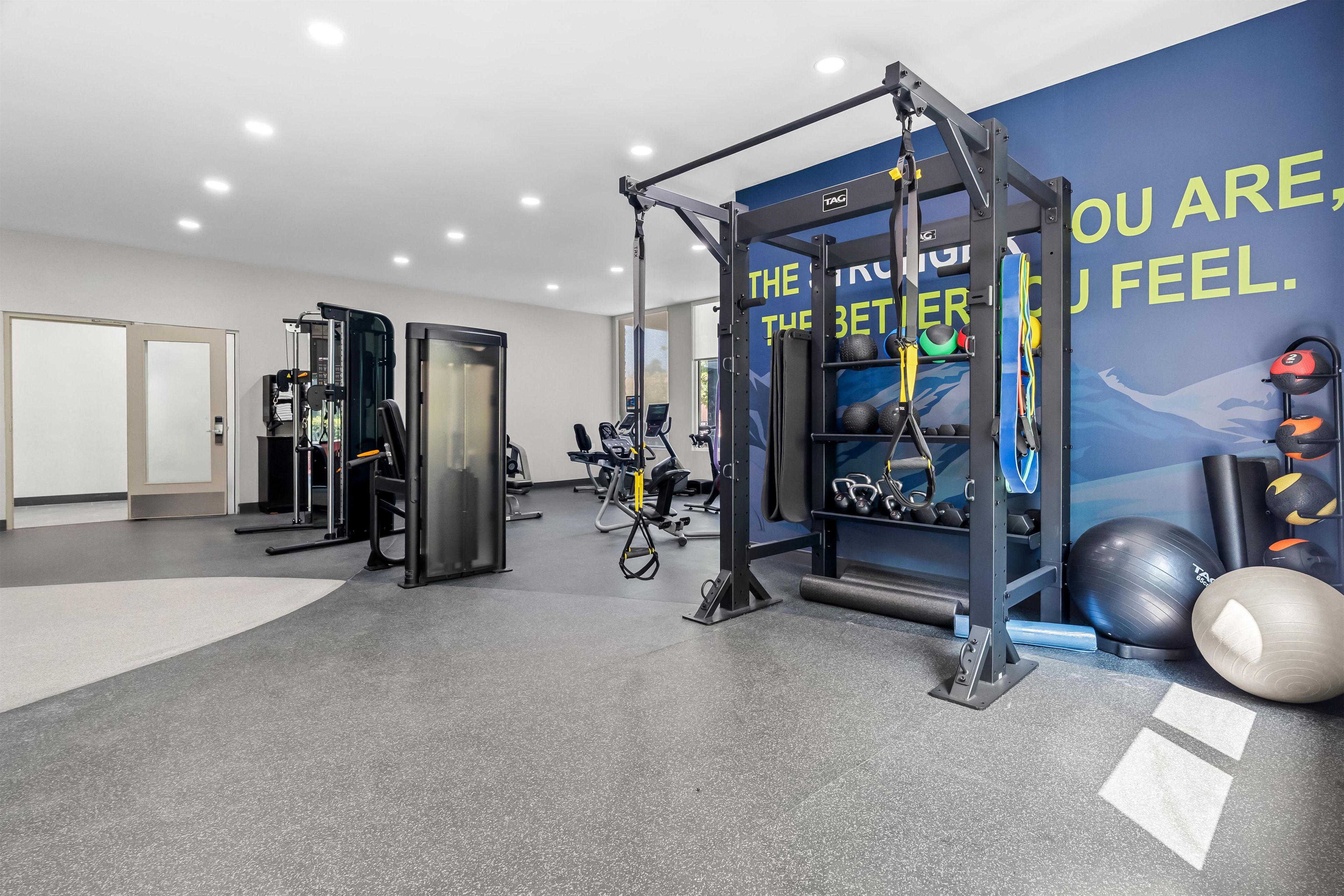 Un gimnasio con equipo de ejercicio diverso, incluyendo una jaula para sentadillas, cintas de correr y pesas sueltas.