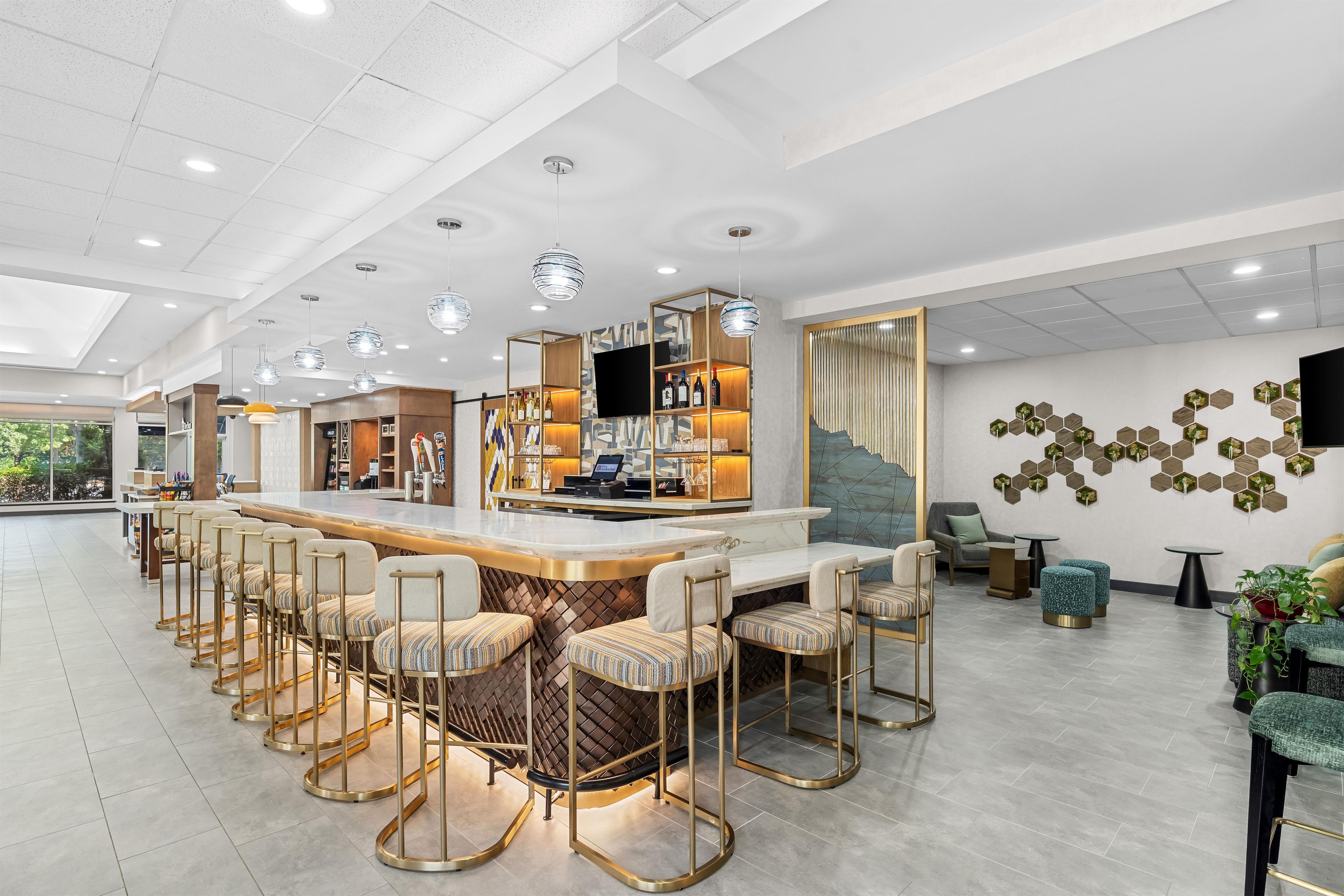 Uma área de bar moderna com um balcão comprido, banquetas e uma tela de televisão.