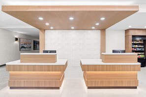 A reception area with two reception desks, a wall with geometric patterns, and a refrigerator stocked with beverages. - Hilton Garden Inn Gainesville (Gainesville)