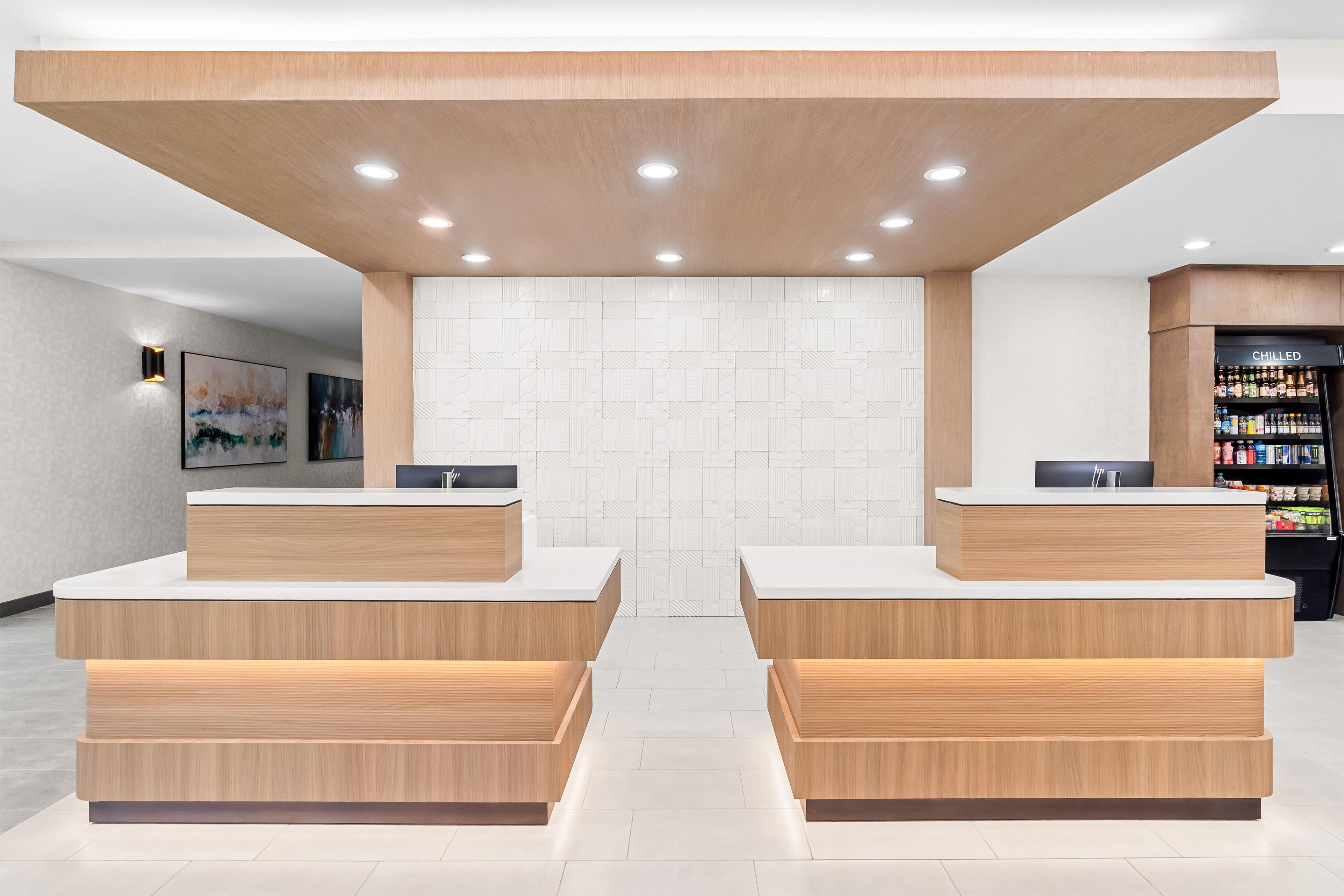 Zona de recepción con dos mostradores, una pared con diseños geométricos y un refrigerador lleno de bebidas.