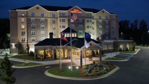 Een meerlaags hotel met een opvallende ingang, vlaggenmast en een goed verlichte gevel.
