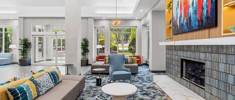 A modern lobby with a sofa, armchairs, a coffee table, a fireplace, and a large abstract painting.