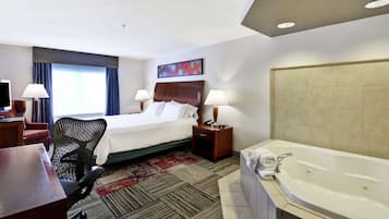 A hotel room with a bed, desk, chair, lamps, and a large bathtub.