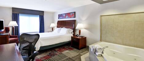A hotel room with a bed, desk, chair, lamps, and a large bathtub.