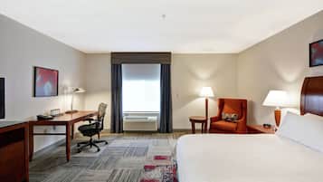 Une chambre d’hôtel avec un grand lit, un bureau avec une chaise, une petite table avec une lampe et une chaise avec un coussin.
