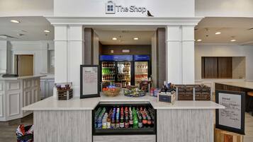 A counter with a beverage cooler, a sign for 'The Shop', and a display of local delicacies.
