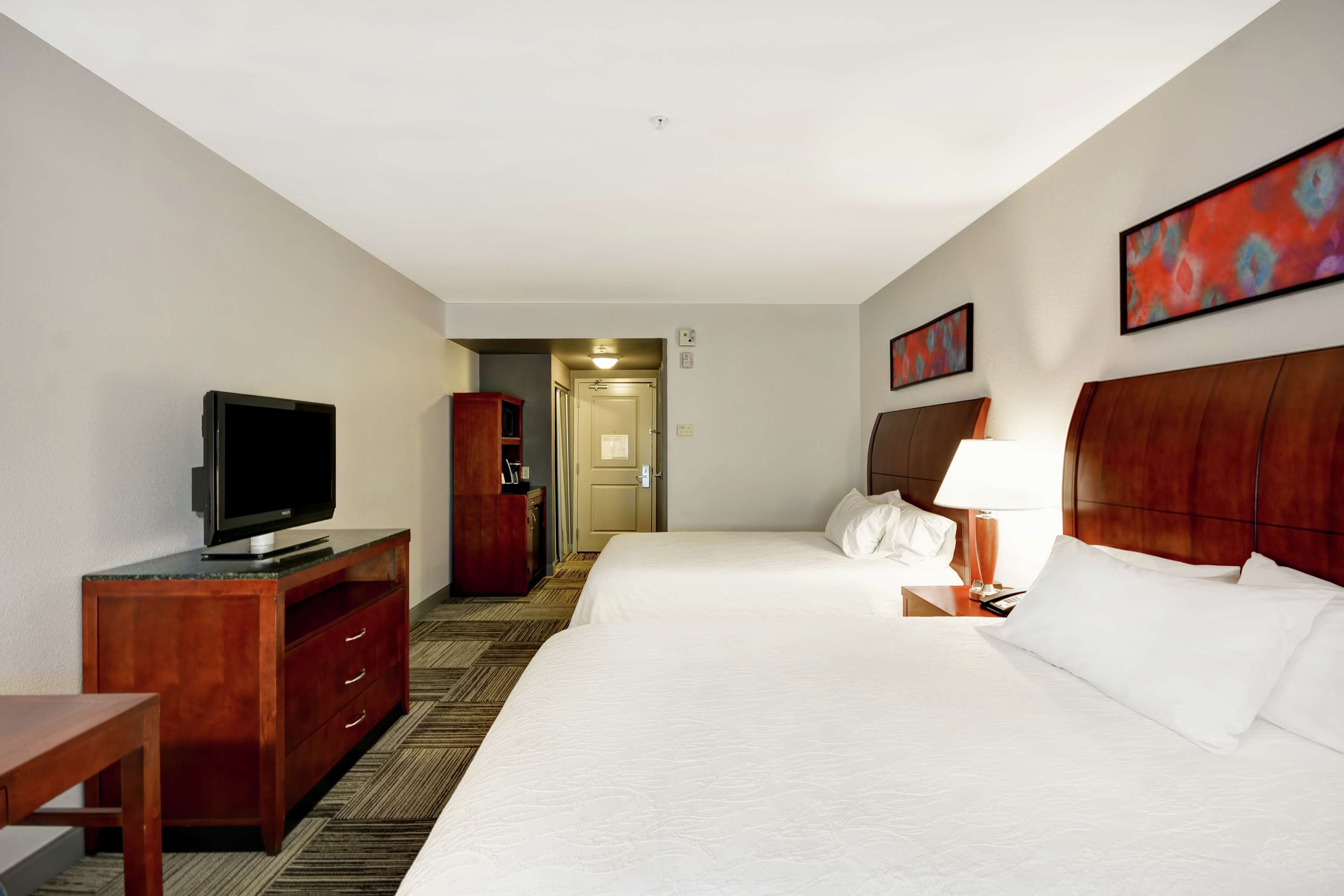 Una habitación de hotel con una cama grande, un televisor sobre un aparador de madera, un escritorio y una lámpara.