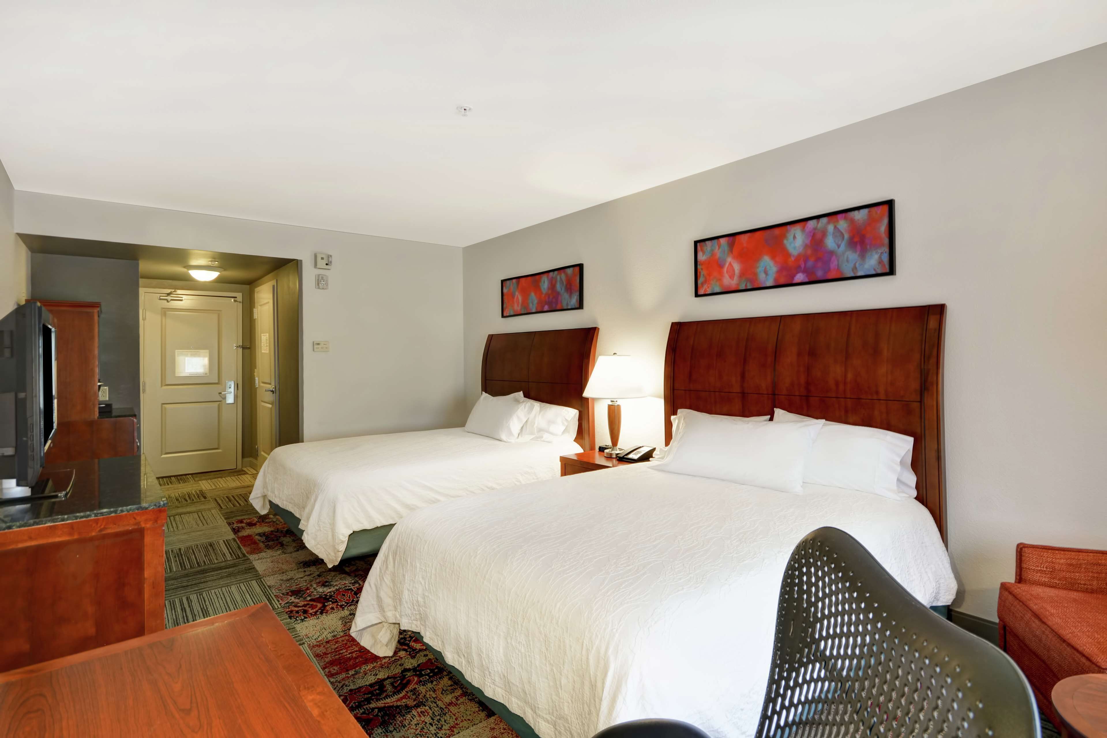 Quarto de hotel com duas camas, uma escrivaninha, uma cadeira e uma televisão.