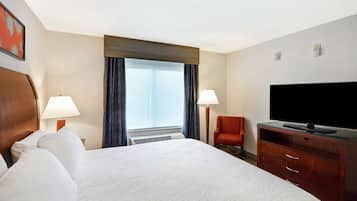 Una habitación de hotel con una cama grande, dos lámparas de noche, un televisor de pantalla plana, un aparador de madera y una ventana con cortinas.