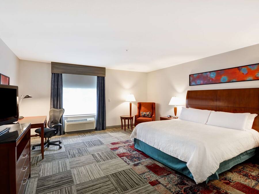 Quarto de hotel com uma cama grande, uma escrivaninha com computador, televisão e uma cadeira.
