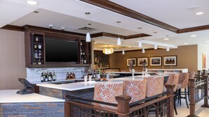 A bar area with a counter, bar stools, and a large screen. - Hilton Garden Inn Columbus/Edinburgh (Edinburgh)