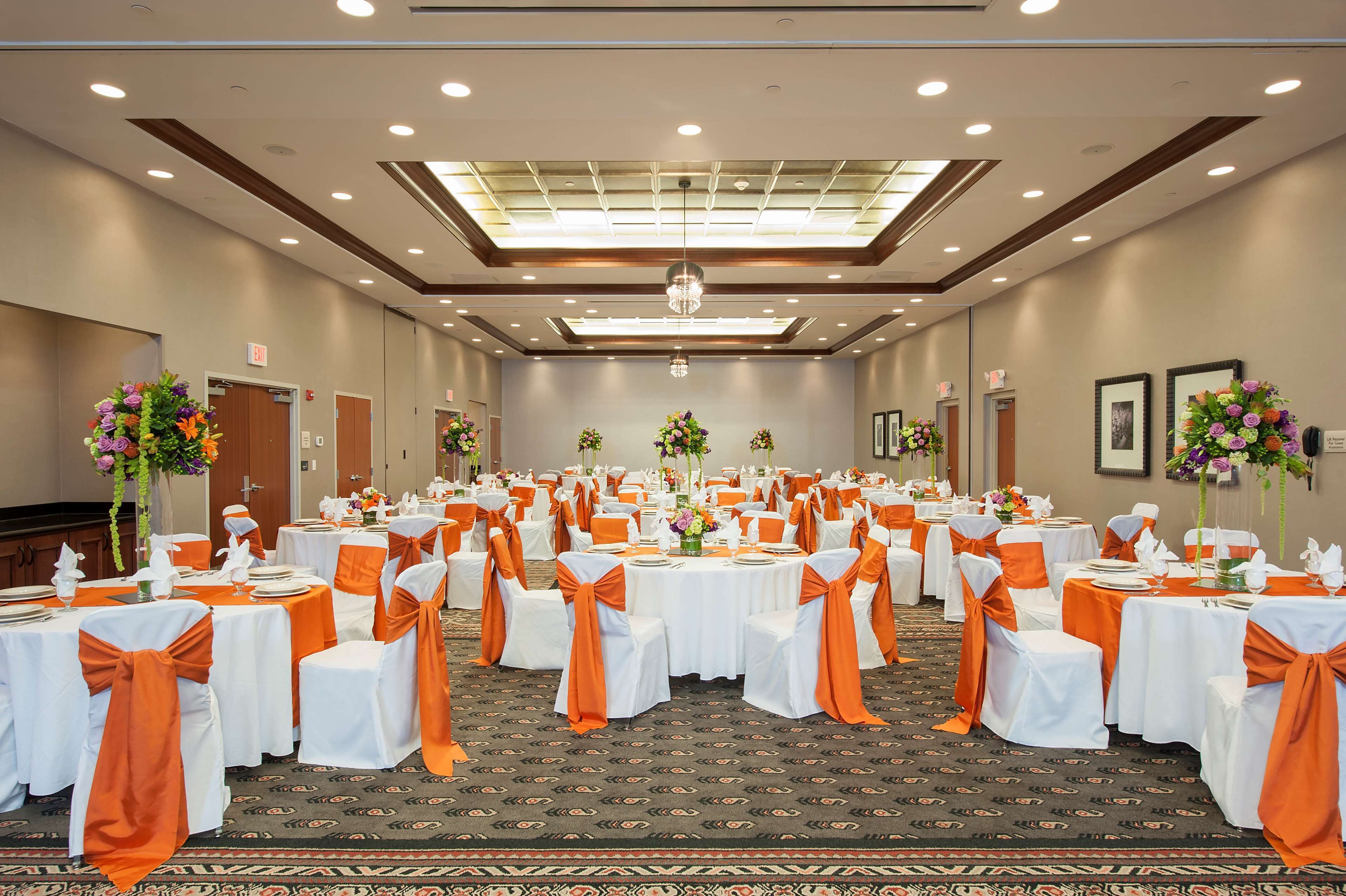 A banquet hall with round tables, white tablecloths, and orange sashes.