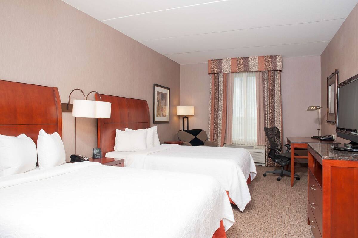 Une chambre d’hôtel avec deux lits, un bureau, une chaise, une télévision et une fenêtre avec des rideaux.
