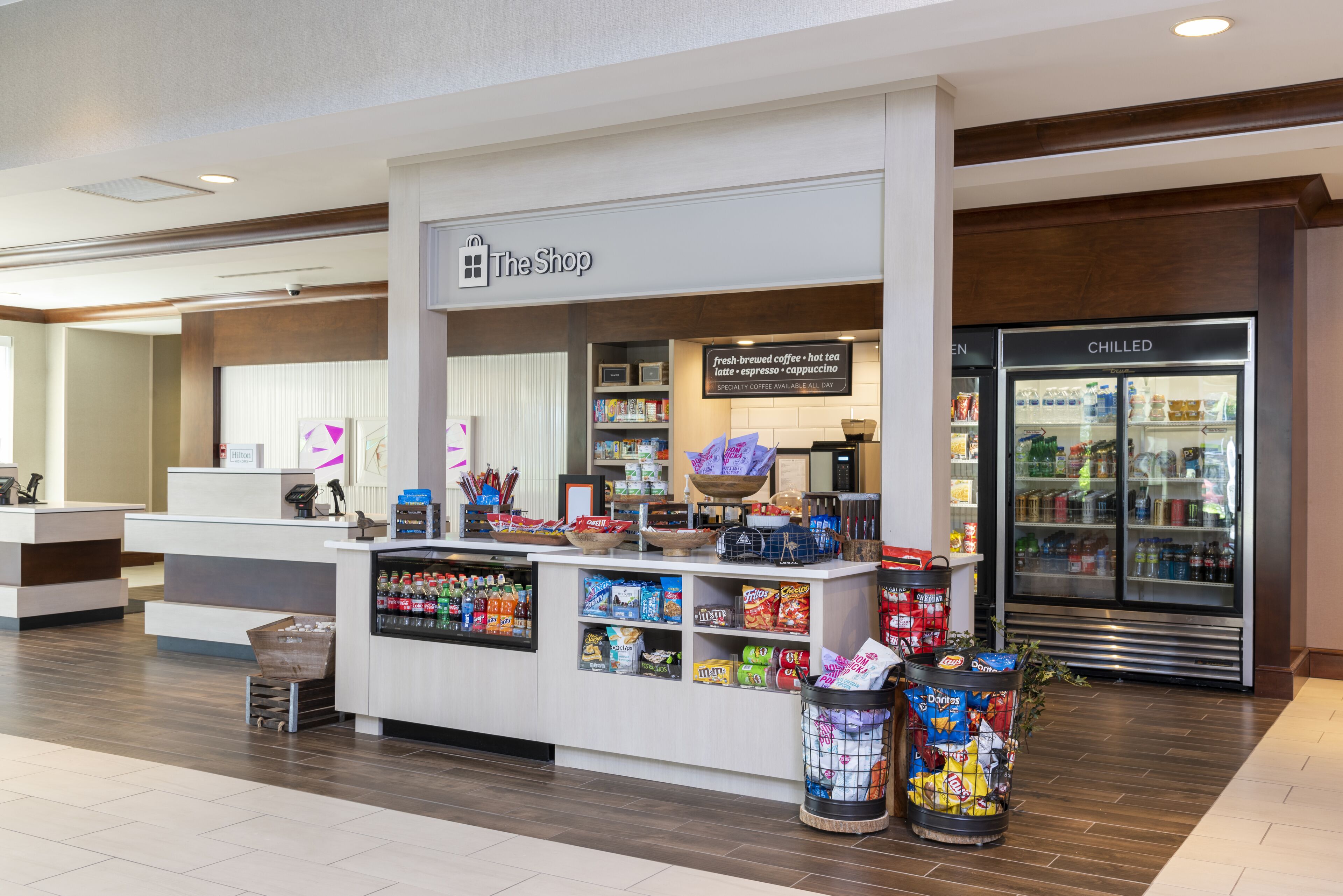 A hotel lobby with a coffee shop named "The Shop" featuring a variety of snacks and beverages.