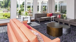 A modern lounge area with a sofa, a round coffee table, and a seating area with a view of the garden. - Hilton Garden Inn Columbus/Edinburgh (Edinburgh)