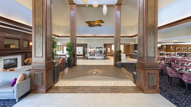A spacious lobby with a central area, wooden columns, a reception desk, and a dining area with tables and chairs. - Hilton Garden Inn Columbus/Edinburgh (Edinburgh)