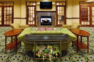 Una habitación con chimenea, dos sillones, un sofá, un televisor y alfombra estampada.