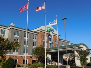 A Holiday Inn Express building with multiple flags, including the American flag and a state flag, and a clear blue sky. - Holiday Inn Express & Suites Millington by IHG (Millington)