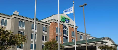 A hotel with a clear sky, multiple flags, and a gas station canopy.