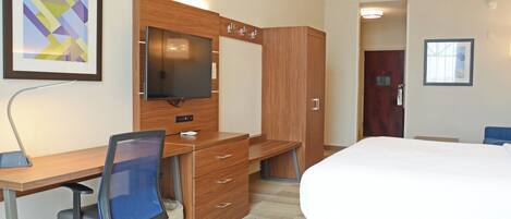 A hotel room with a wooden desk, a chair, a bed, a TV, and a wardrobe.