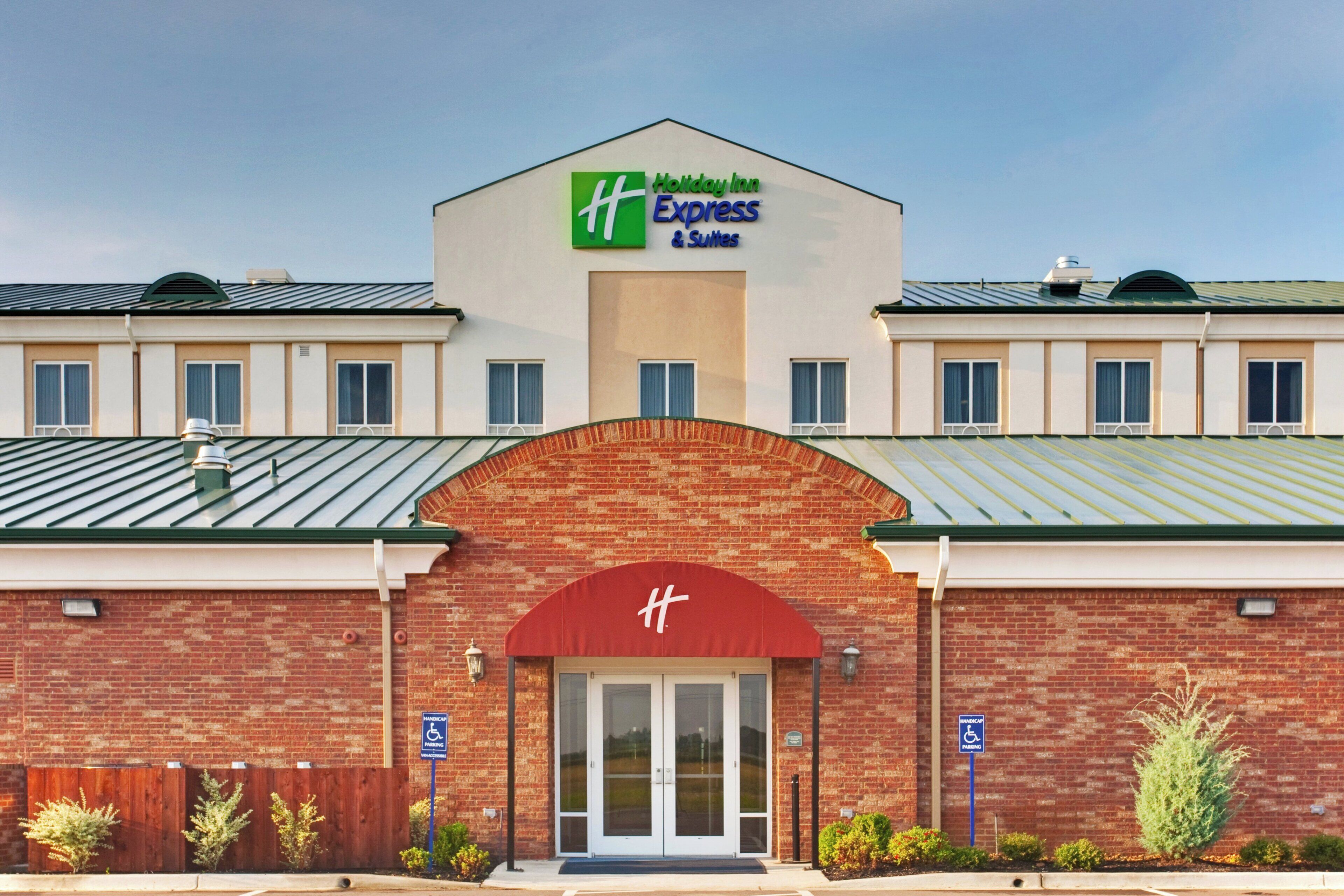 A Holiday Inn Express & Suites building with a brick facade, large entrance, and handicap parking signs.