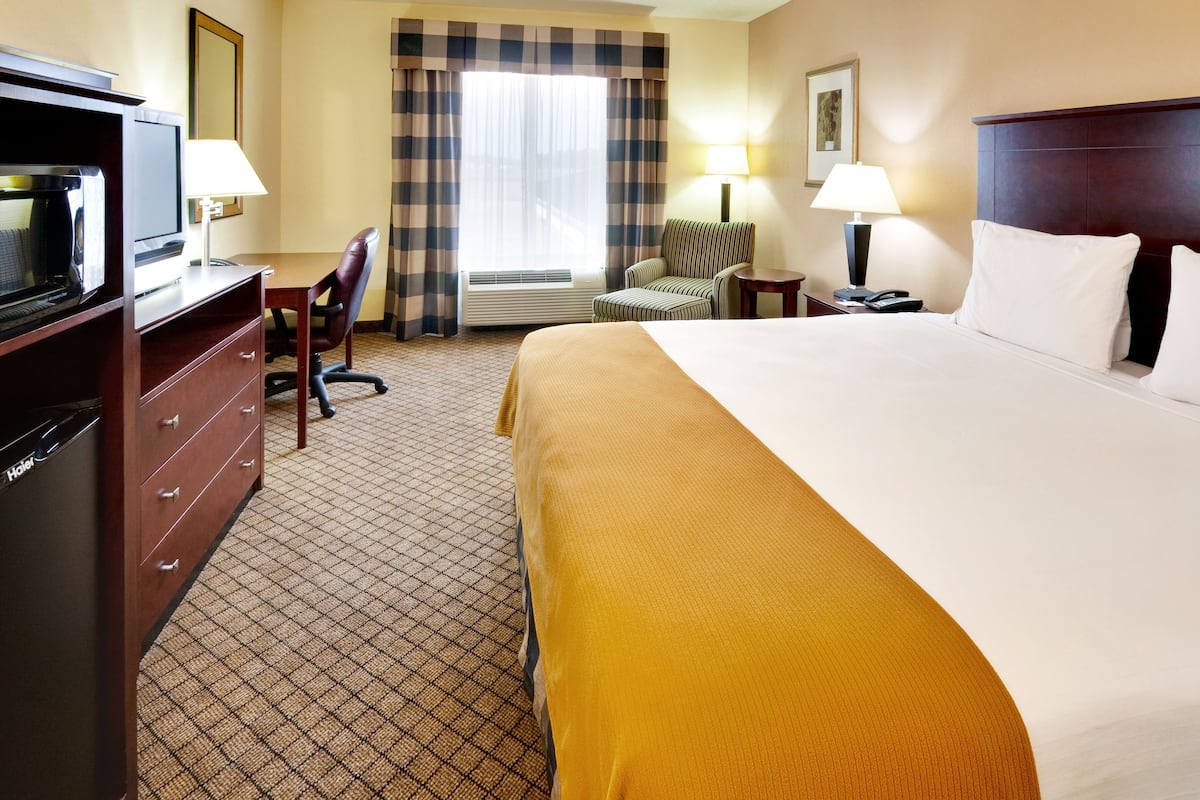 A hotel room with a bed, a desk with a television, a chair, a lamp, and a nightstand with a phone.