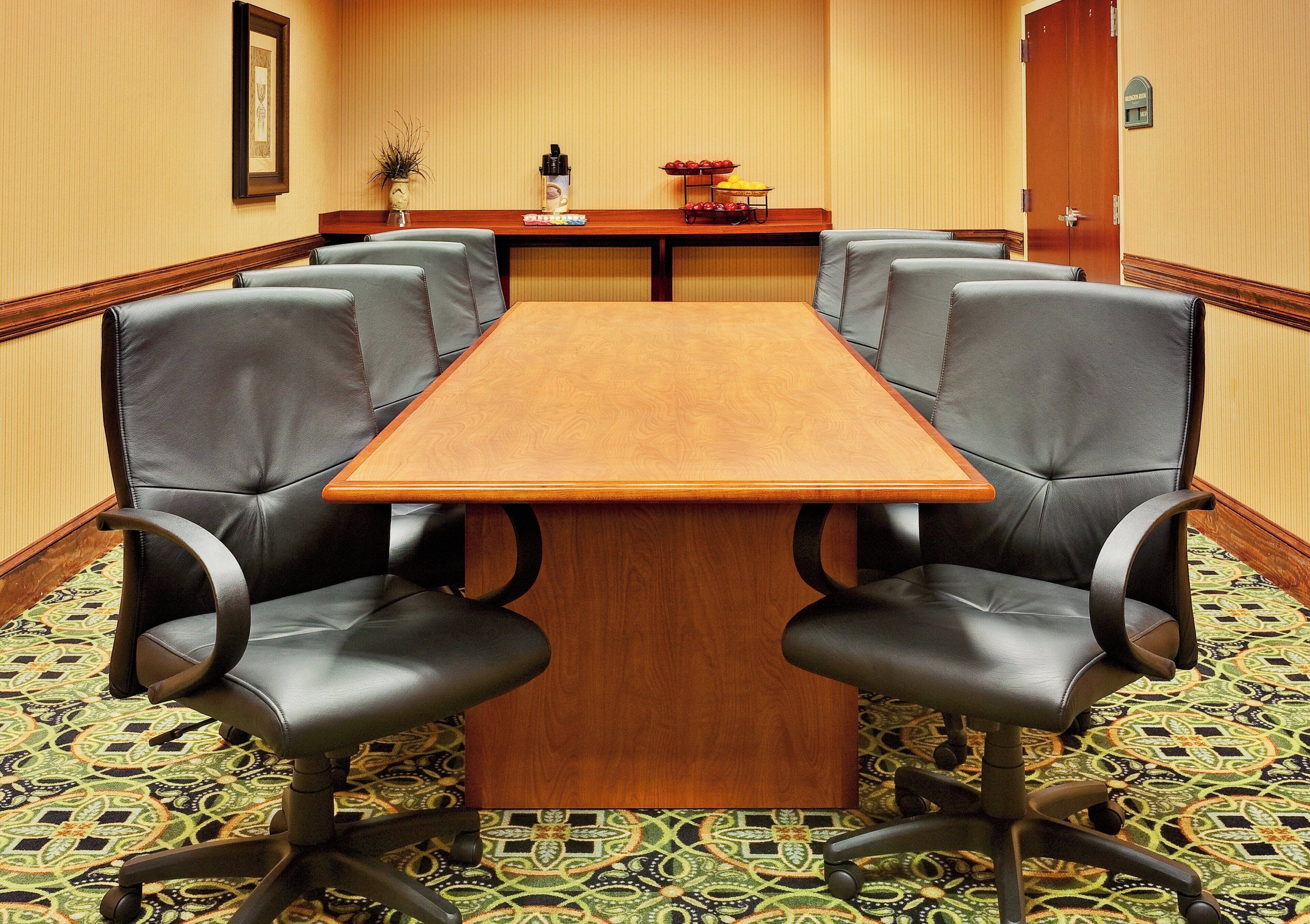 Un salón de conferencias con una mesa de madera y cuatro sillas de cuero.