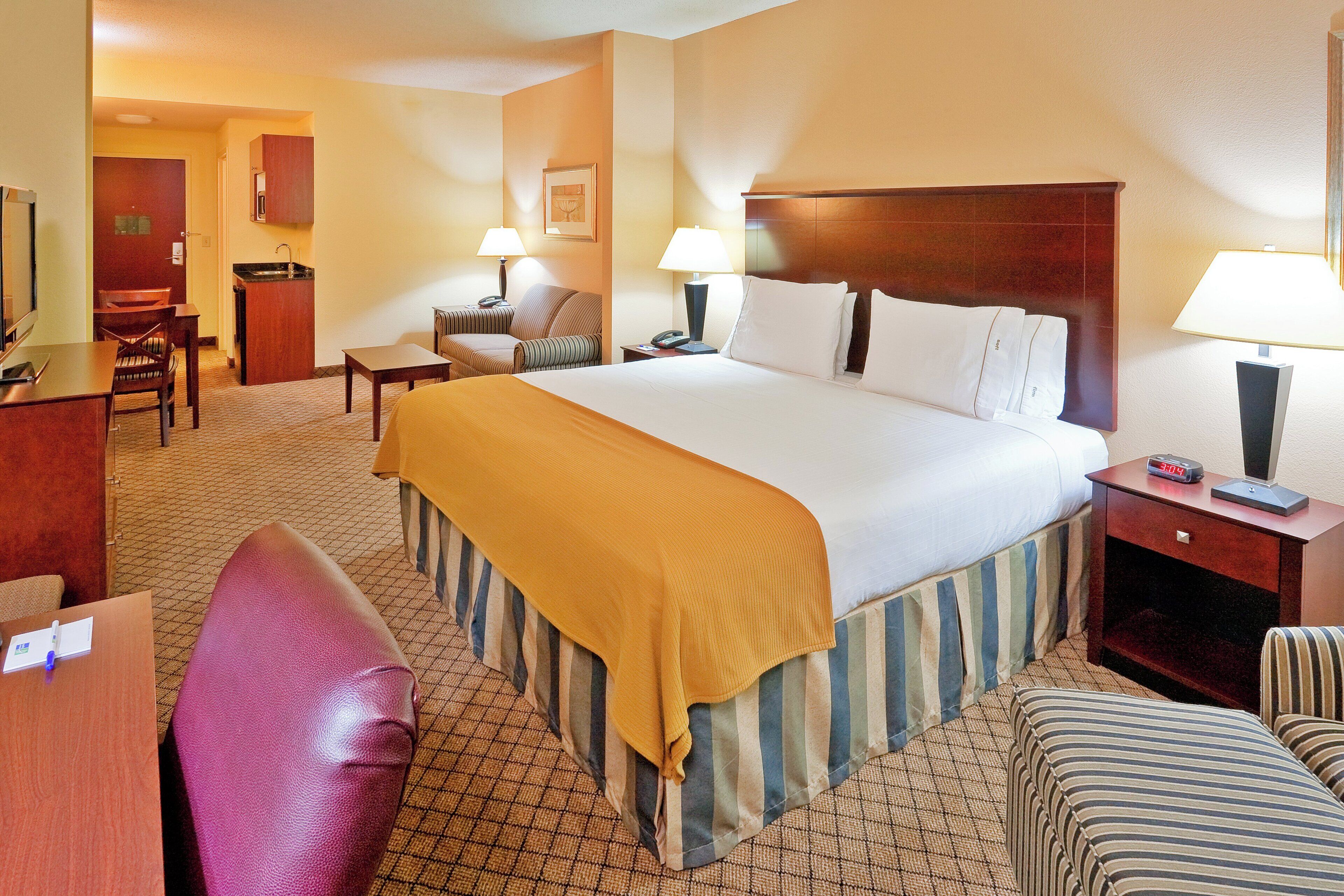 A hotel room with a large bed, a desk, a chair, and a small table.