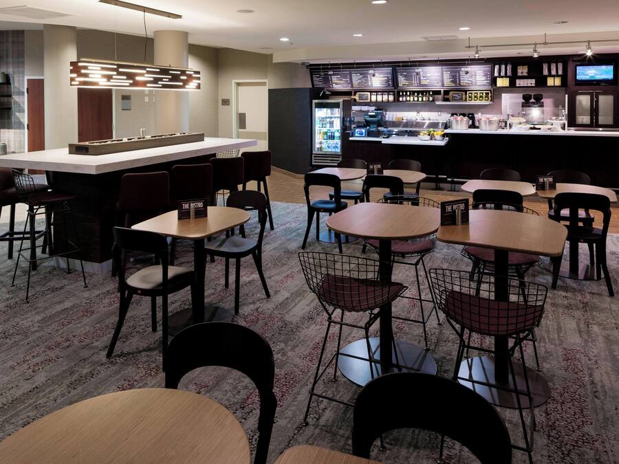 Un restaurante moderno con una zona de bar, diversas opciones de asientos que incluyen mesas y sillas, y un tablero de menú visible.