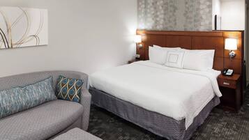 Una habitación de hotel con cama, sofá, mesita de noche y lámpara de pared.