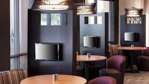 Ein modernes Interieur mit runden Tischen, gepolsterten Sitzmöglichkeiten, einem wandmontierten Flachbildfernseher und natürlichem Licht durch große Fenster.