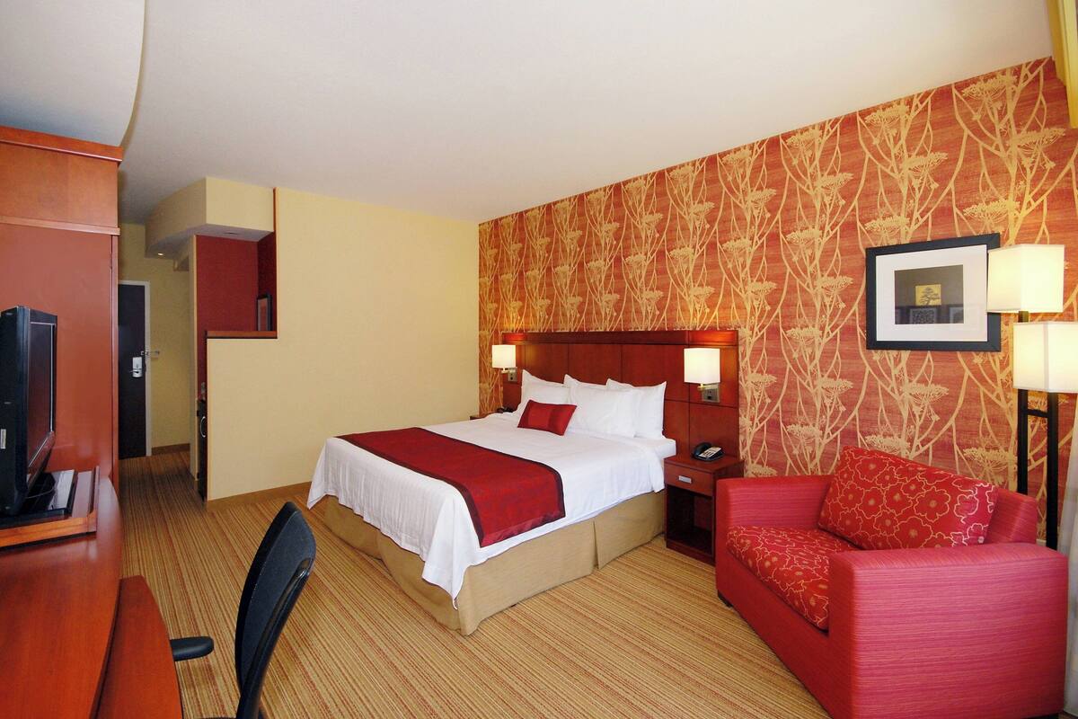 A hotel room with a bed, a red sofa, a desk, and a television.