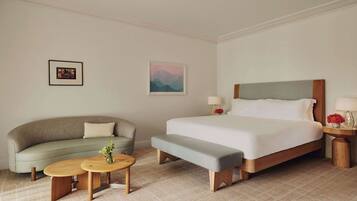 A hotel room with a bed, a sofa, a bench, two small tables, and a picture on the wall.