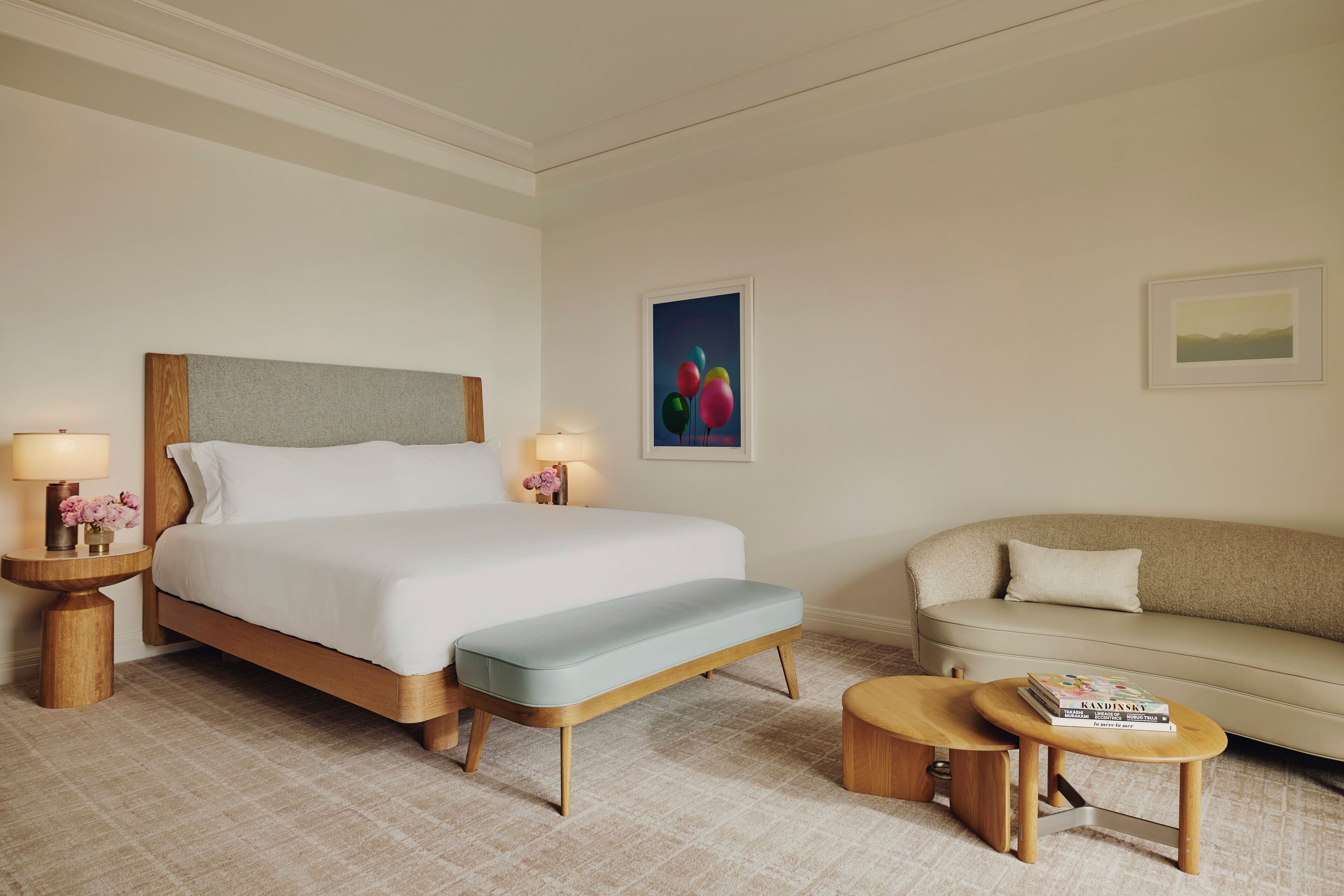 A hotel room with a large bed, a bench, a sofa, and a small table with books.
