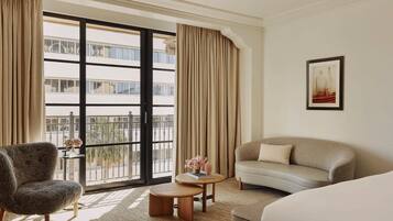 Habitación de hotel con un ventanal grande, un sofá, una silla, una mesita redonda y una cama.