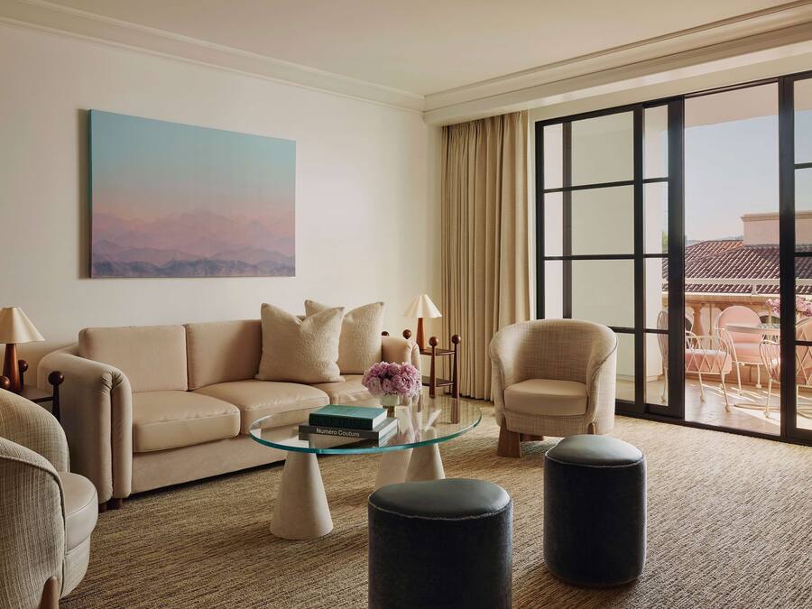 Una sala de estar moderna con un sofá color beige, una mesa de centro de vidrio y un ventanal con vista a un edificio.