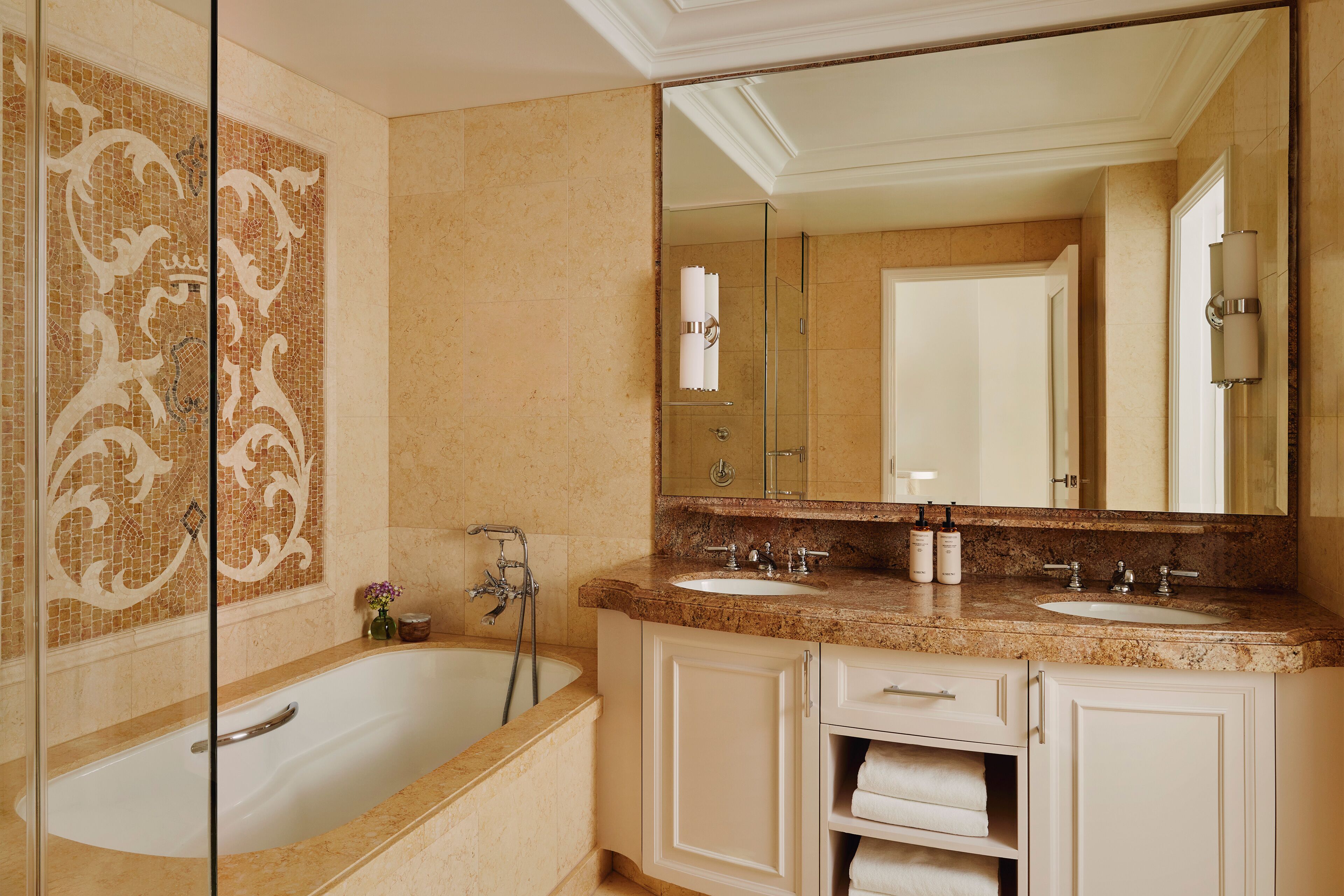A bathroom with a large bathtub, two sinks, a vanity with drawers, and a large mirror.