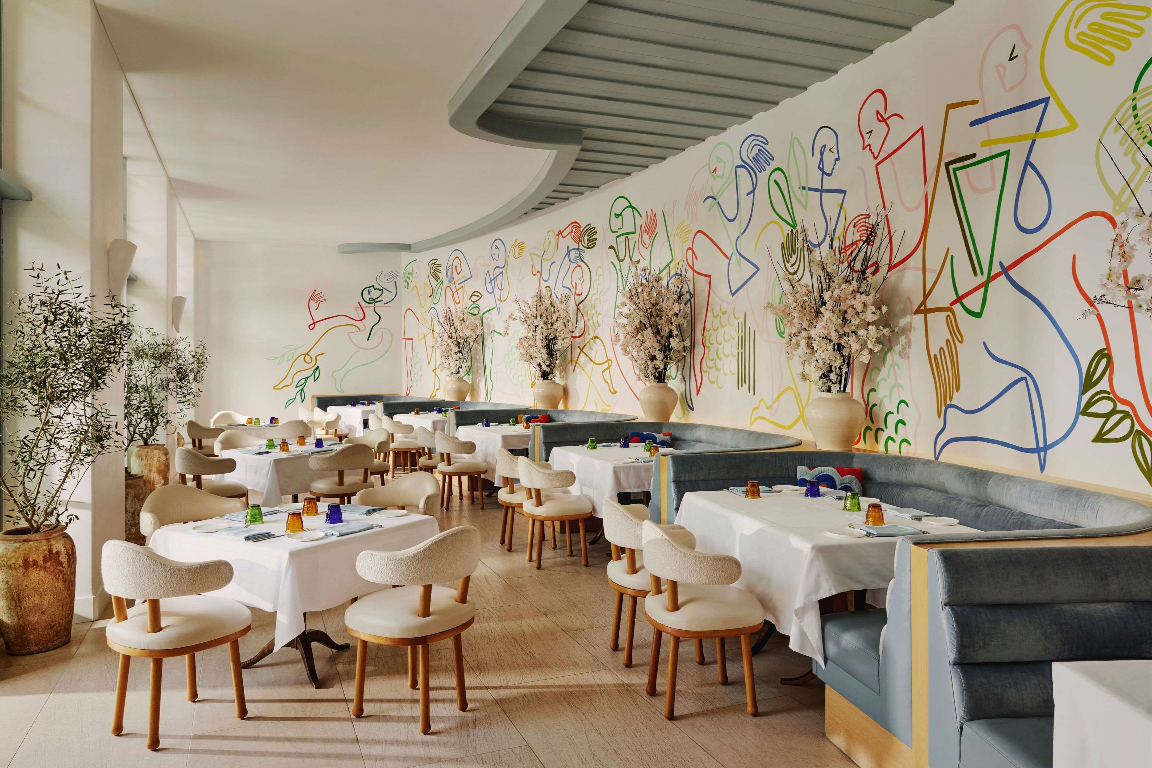 A restaurant with white tables and chairs, a curved ceiling, and abstract wall art.