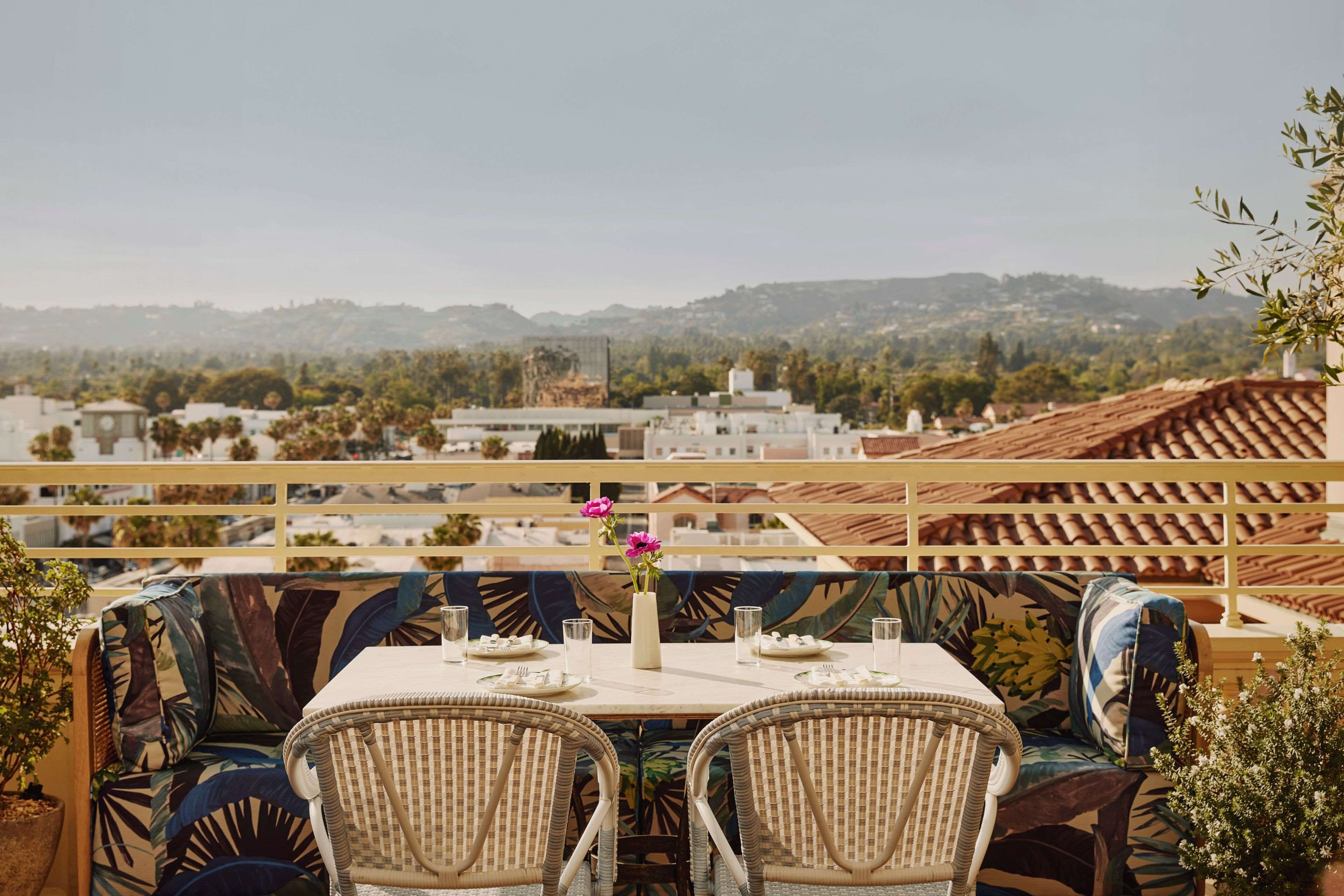 A terrace with a table set for two, overlooking a scenic view of buildings and hills.