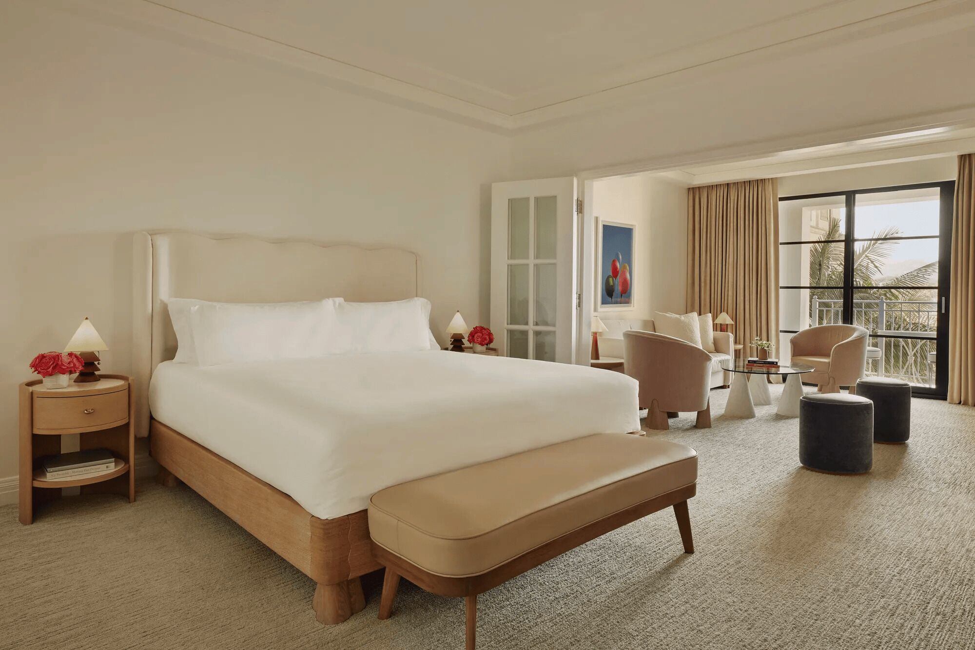 A hotel room with a large bed, a sitting area with chairs, a small table, and a view of the outdoors.