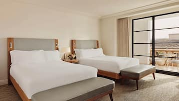 A hotel room with two beds, a small table with a lamp, and a view of the city through large windows.