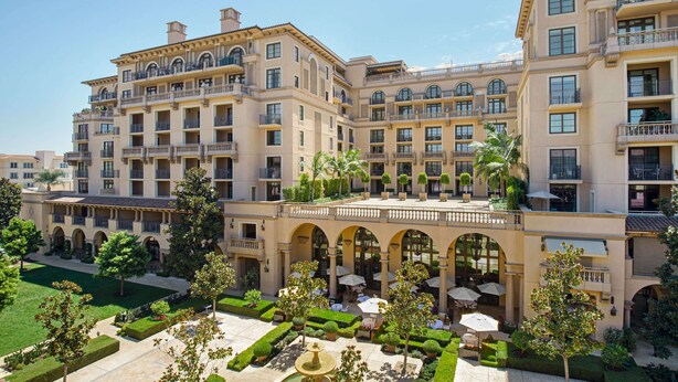 A large, multi-story hotel with a central courtyard, outdoor seating areas, and a well-maintained garden.
