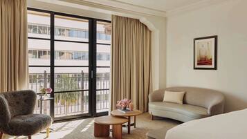 A hotel room with a large window, a sofa, a chair, a small table with flowers, and a framed picture on the wall.