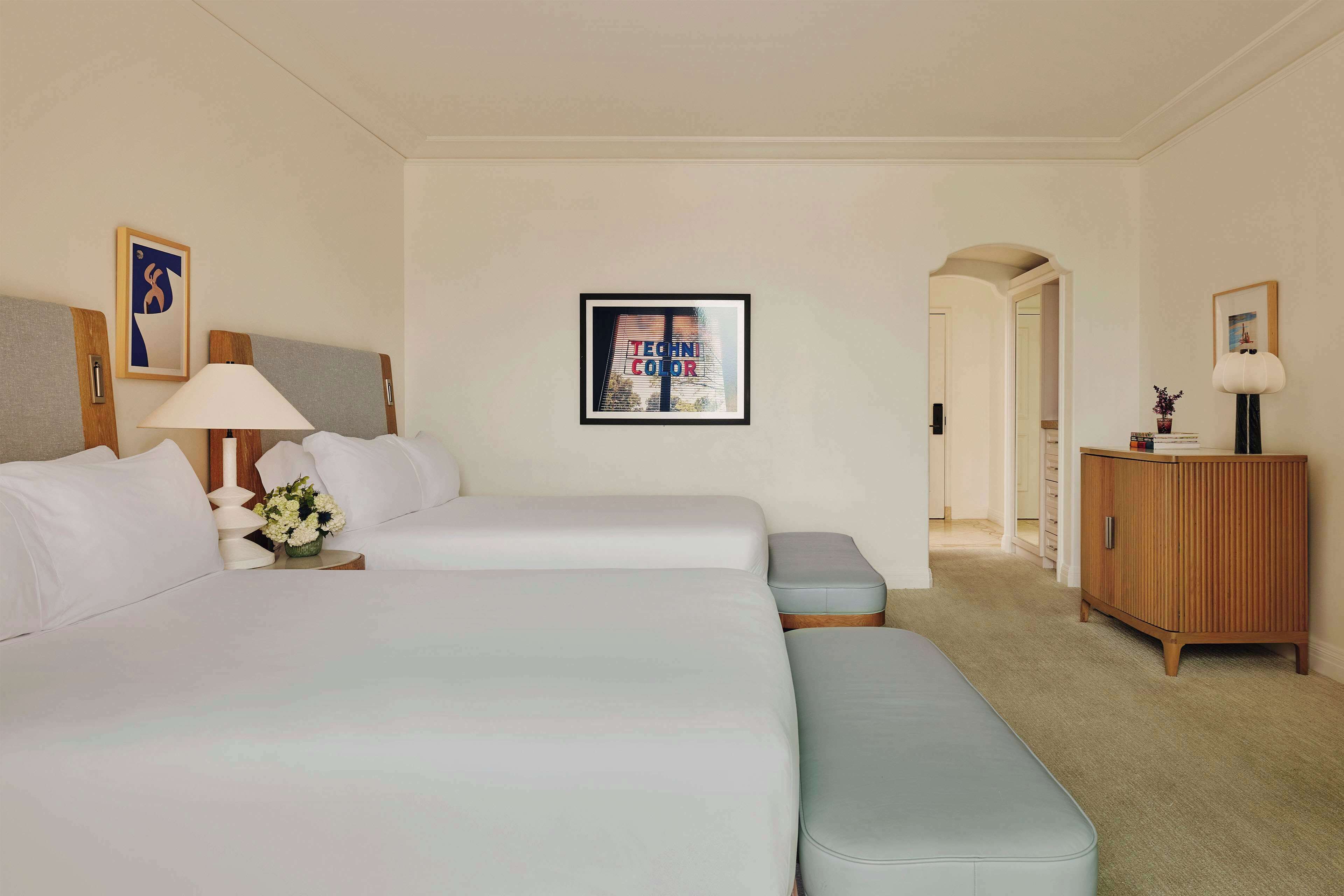 A hotel room with two beds, a bedside table with a lamp, a framed picture on the wall, and a wooden cabinet.
