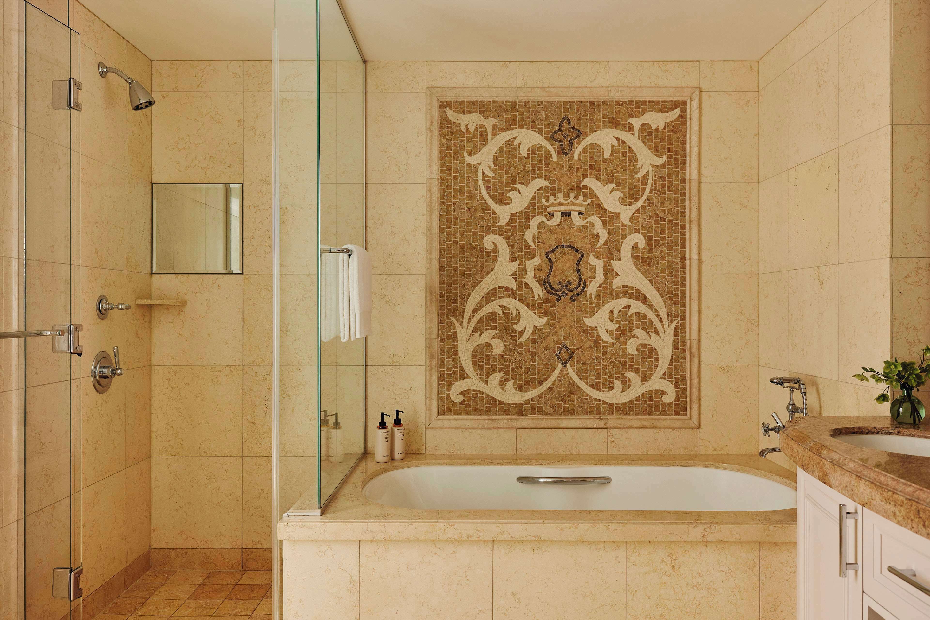 Een badkamer met een groot bad, een glazen douchecabine, een decoratieve betegelde muur en een wastafel met spiegel.