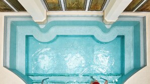 A large indoor swimming pool with a tiled floor and a person swimming.