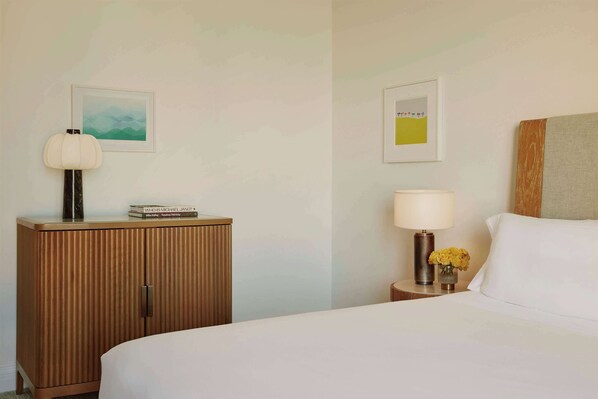Une chambre d’hôtel avec un lit, une armoire en bois, deux tables de chevet et des œuvres d’art encadrées accrochées aux murs.