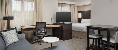 A hotel room with a sofa, a desk with a computer, a TV, a bed, and a small table with two chairs.